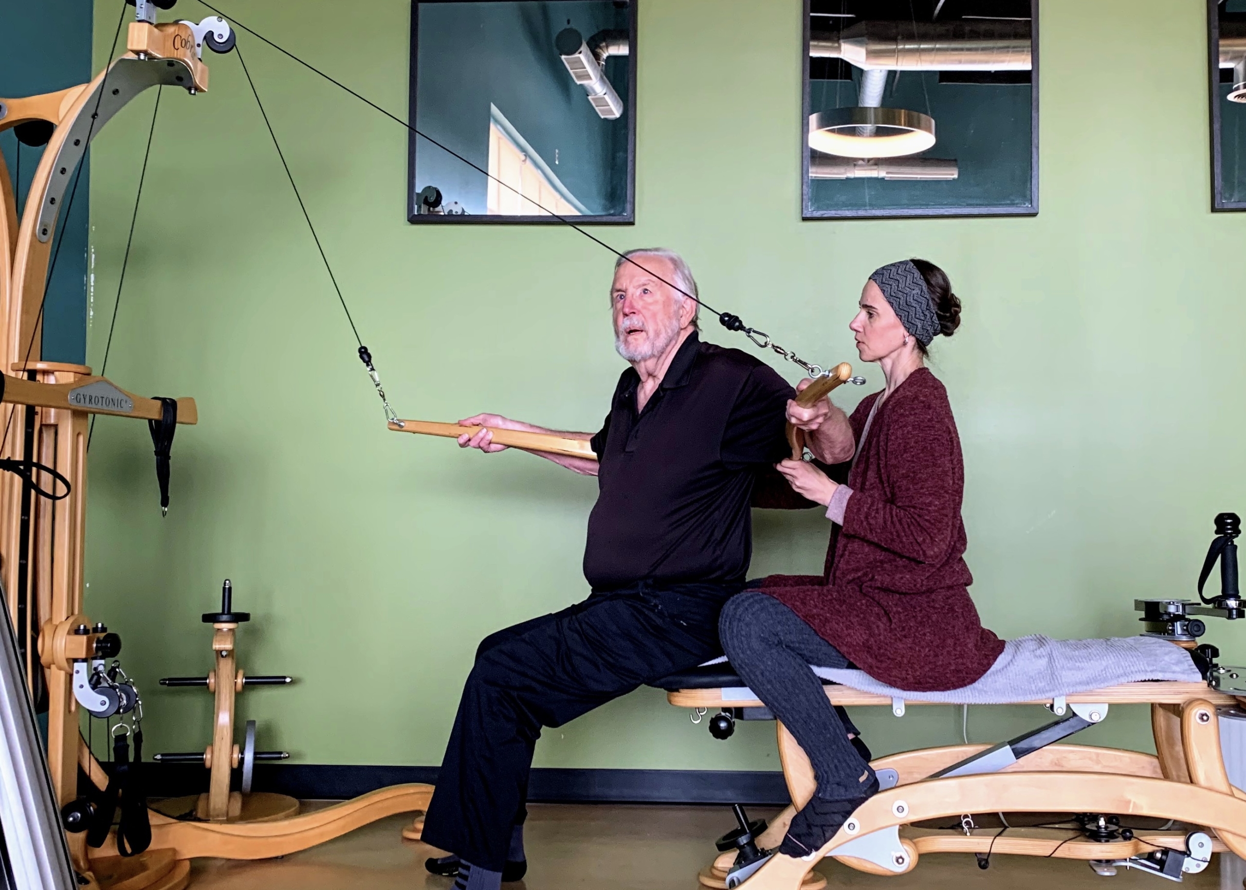 An older gentleman working out with a private trainer on the GYROTONIC Tower